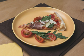 close up view of piece of italian pizza with cherry tomatoes on plate