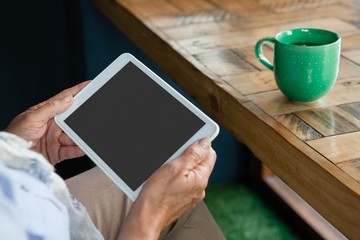 Close up of senior  woman holding tablet against coffee cup on