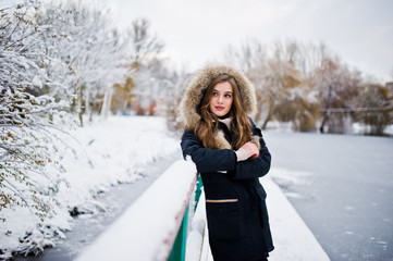 Fototapeta na wymiar Beautiful brunette girl in winter warm clothing. Model on winter jacket against frozen lake at park.