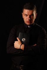 Young priest holding and crypto bible with bitcoin logo on the dark background