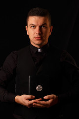 Young priest holding and crypto bible with bitcoin logo on the dark background
