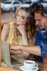 Couple using digital laptop while sitting at cafe shop