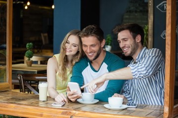 Happy friends looking at smart phone while sitting by table