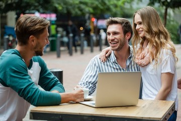 Cheerful couple looking at friend while sitting at sidewalk cafe