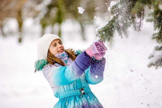 Little girl shaking the branch of pine tree covered by snow.