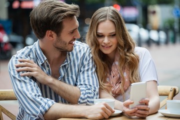 Couple using mobile phone while sitting at sidewalk cafe