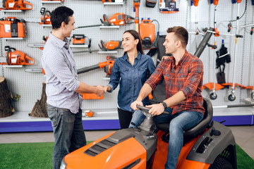 A consultant in a garden tools store shows a customer a lawn mower.