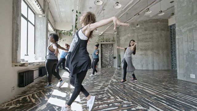 Zoom out of young female dance instructor and multiethnic group of women rehearsing choreography in airy studio
