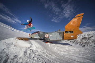 Snowboarding jump over plane in snowpark winter mountains