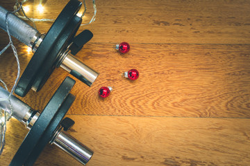 Top view of black metal fitness weights on wooden background with shining Christmas lights and red decorations, holidays and fitness concept