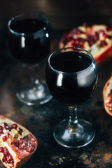 Fresh pomegranate wine in glass on black rustic surface.