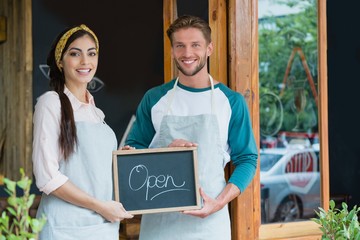 Portrait of smiling waiter and waitress standing with chalkboard