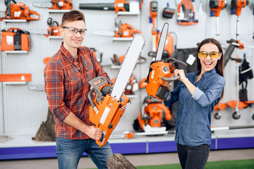 A guy and a girl are posing on the camera with chainsaws in their hands.
