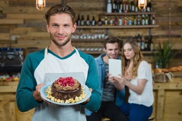 Portrait of waiter holding plate of cake and customer in