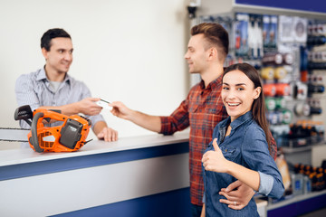 The guy and the girl pay for the purchase of a chainsaw.