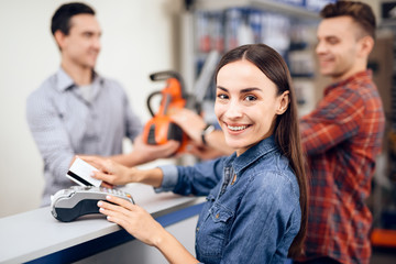 The guy and the girl pay for the purchase of a chainsaw.