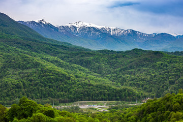 The mountain range of the Caucasus with a snowy peak in the spring with a bright green forest. Mountain valley on the way to Krasnaya Polyana from Adler, Sochi, Russia.
