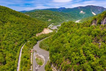Fototapeta premium A colorful spring green forest on the slopes along the banks of the Mzymta River flowing near the road. Mountain valley on the way to Krasnaya Polyana from Adler, Sochi, Russia.