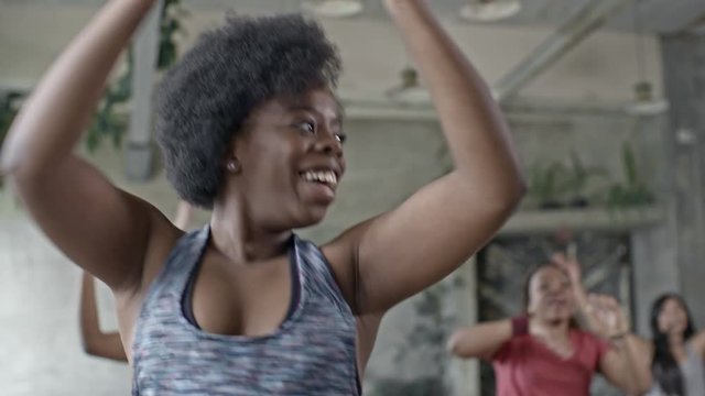 Medium shot of cheerful African woman wearing fitness outfit and headband doing aerobics in group class