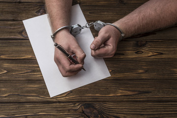 Men's hands with handcuffs fill the police record, confession. on top see the police investigative...