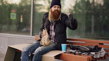 Very drunk homeless man show fuck you sign into the camera and sleeping while sitting on bench at...