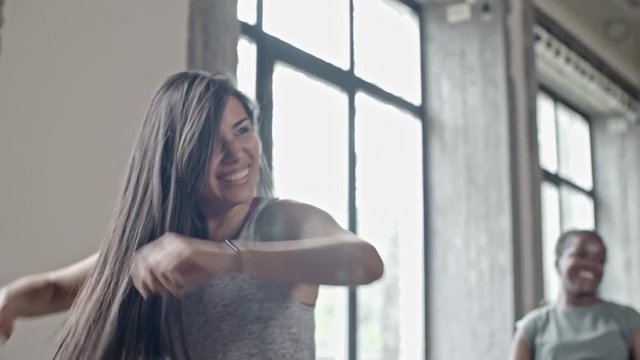 PAN of laughing Hispanic woman dancing in group class and looking at curly female instructor showing zumba moves
