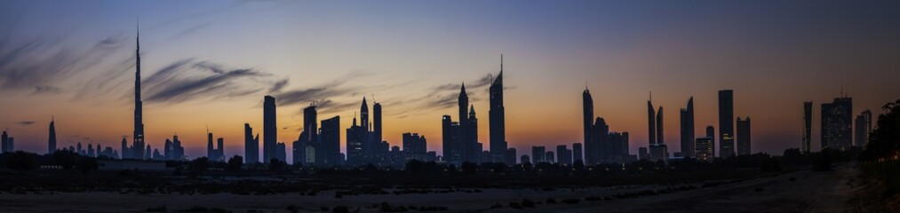 Panorama der Skyline von Dubai mit Silhouette der Wolkenkratzer im Gegenlicht fotografiert Abends...