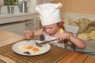 Small girl has a snack. Little girl eats ham and eggs. Cute girl wears chef costume.  Family and childhood concept.