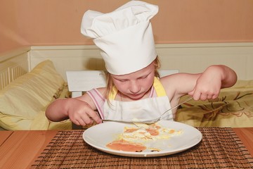 Small girl has a snack. Little girl eats ham and eggs. Cute girl dressed like a chef - white chef costume. Family and childhood concept.