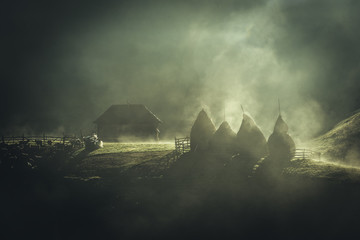 Foggy morning in the Carpathian mountains. Farmi house with haystacks