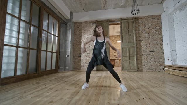 Zoom in shot of happy female dance with curly hair improvising in empty loft
