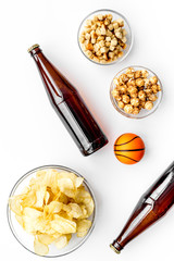 Snacks for watching sport matches and games on TV. Crisps, popcorn, rusks near drink and ball on white background top view