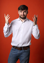 Confused puzzled funny bearded man in white shirt and blue jeans gesturing the hands on bright orange background