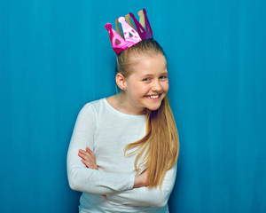 Smiling little girl with paper crown standing with arms crossed.