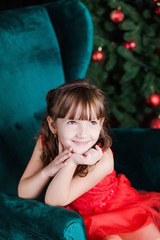 Closeup portrait of cute little girl sitting in green armchair in beautiful Christmas interior. Happy girl dreaming about presents from Santa. Vertical color photography.
