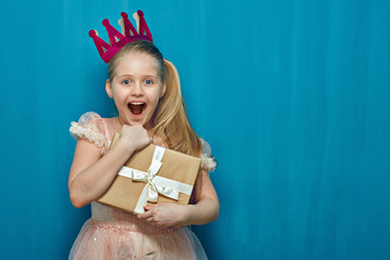 Happy surprising girl wearing pink dress and crown holding gift