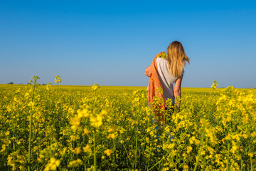 Fototapeta premium Beautiful young woman walking along the field of yellow flowers
