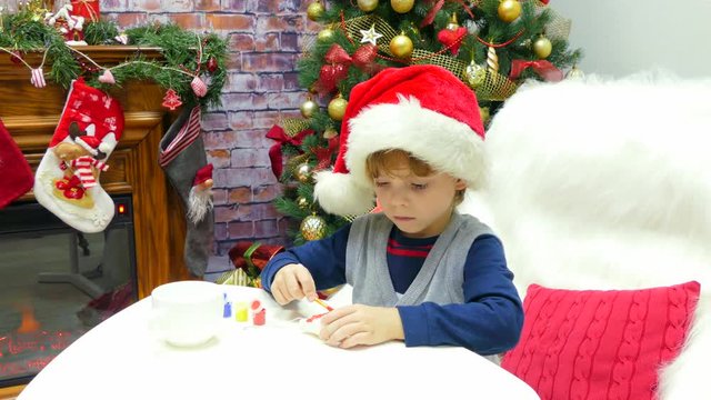 A boy in a santa hat is painting a Christmas toy.