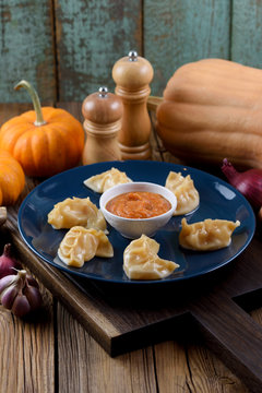Traditional Asian dish. Crescent shape imperfect dumplings with spicy sauce served with garlic, onion and pumpkin on oak board