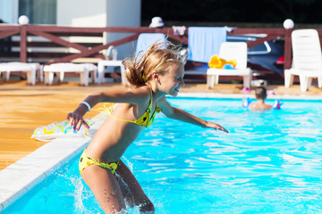 Naklejka premium Happy kid playing in blue water of swimming pool. Little girl learning to swim. Summer vacations concept. Cute girl swimming in pool water. Child splashing and having fun in pool
