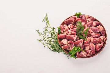 Raw chicken hearts on the plate ready for cooking with rosemary and spices on a white wooden background. Top view. Free space for text.