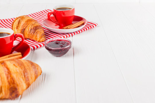 Freshly baked croissant on napkin, cup of coffee in red cup on white wooden background. French breakfast. Fresh pastries for breakfast. Delicious dessert. Closeup photography. Horizontal banner