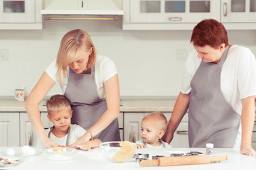 Obraz na płótnie Canvas Cooking gingerbread cookies at home in the white kitchen. Happy family of mother, grandmother and little kids boys in the kitchen. Mom, grandma and children sons cooking together