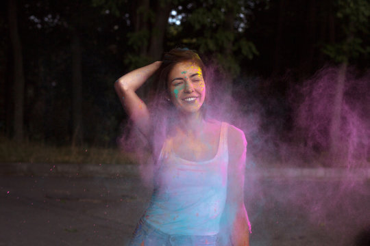 Cheerful tanned woman with short hair posing with exploding Holi pink dry powder