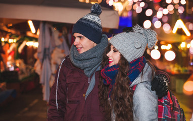 Young couple walking at evening on traditional Christmas market, fairy place