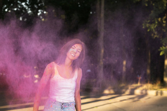 Adorable tanned woman with short hair posing with exploding Holi purple paint