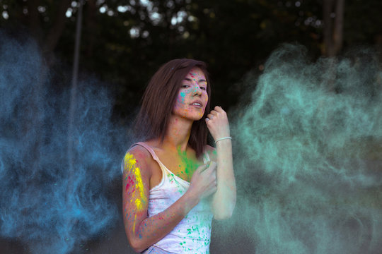 Glorious young woman with short hair posing with exploding Holi blue and green dry paint