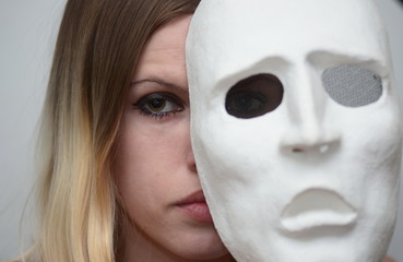 blonde girl with closed eyes holds a white theatrical mask