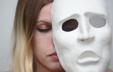 blonde girl with closed eyes holds a white theatrical mask