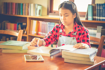 Girl is using tablet while sitting in library and reading a book